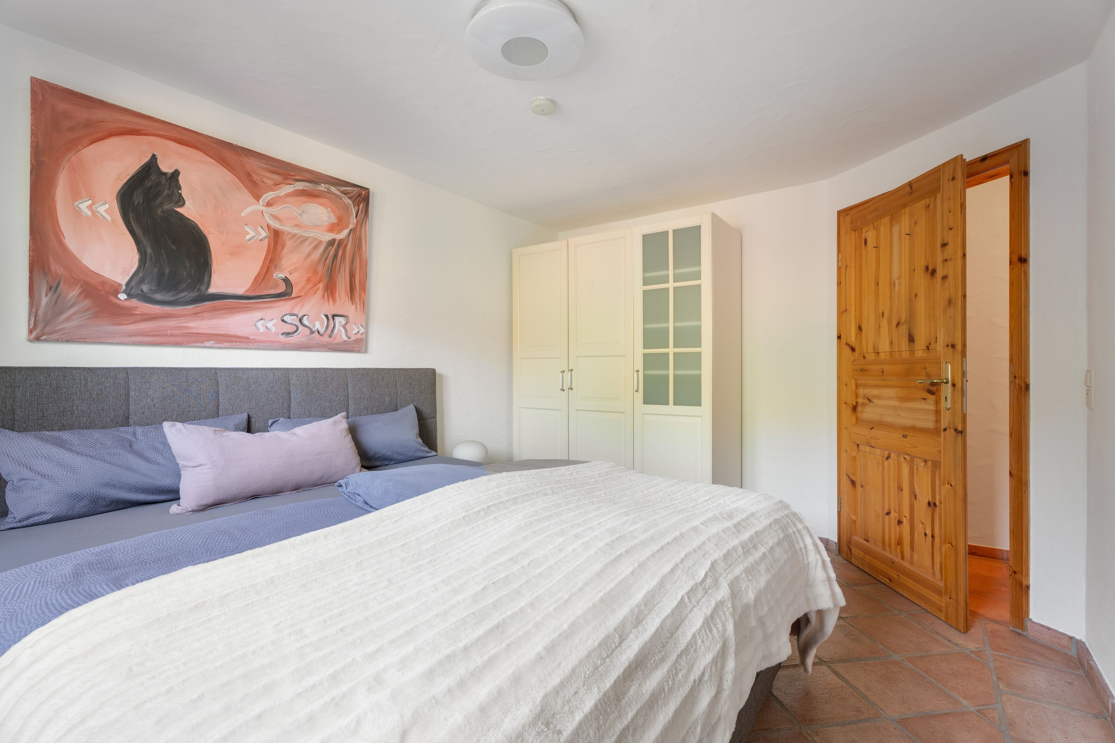 Un dormitorio con una cama, un cuadro, un armario y una puerta de madera.