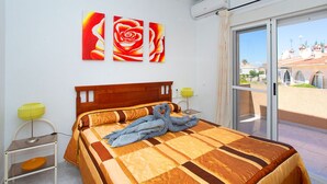 Une chambre à coucher avec un grand lit, une vue sur un immeuble à travers une porte vitrée et un mur orné de trois tableaux représentant des roses.