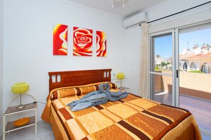A bedroom with a large bed, a view of a building through a glass door, and a wall with three rose paintings. - CH Logroño Doña Pepa (Ciudad Quesada) (Ciudad Quesada)