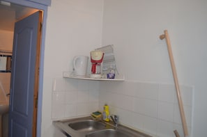 A kitchen with a sink, a coffee maker, a dish rack, and a broom leaning against the wall.