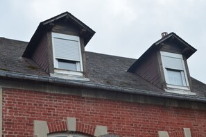 A two-story building with a red brick facade, dormer windows, and a visible chimney.