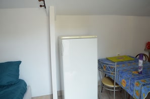 A room with a bed, a white refrigerator, a table with a floral tablecloth, and a chair.