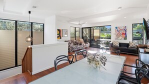 A spacious living area with a dining table, chairs, a sofa, and artwork on the walls. - Straddie Beach House 2 | Bush & Beach Retreat (Point Lookout)