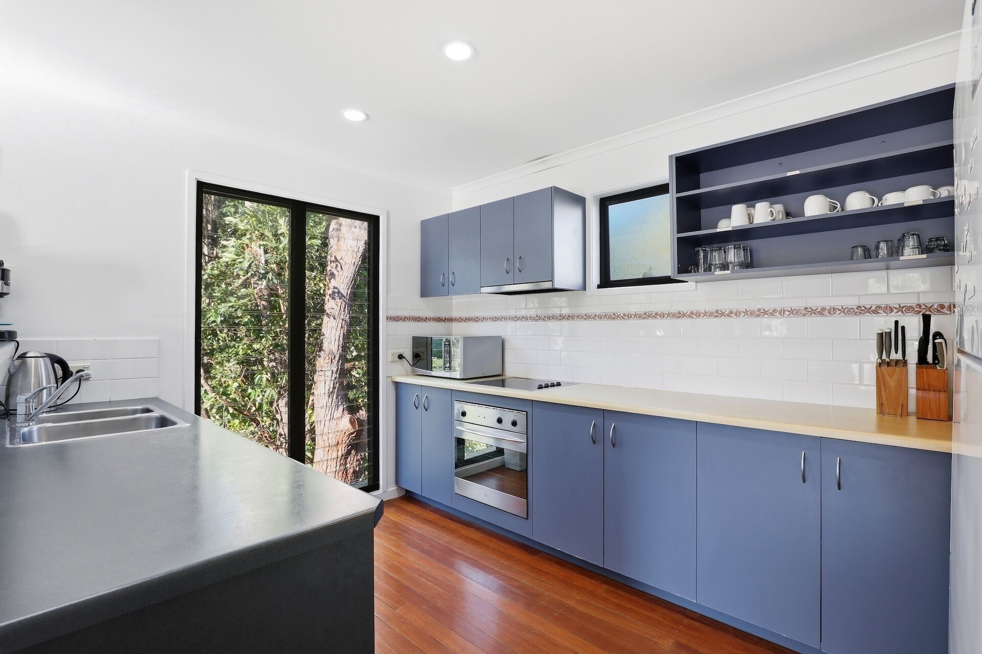 A modern kitchen with blue cabinets, a built-in oven, a microwave, and a sink.