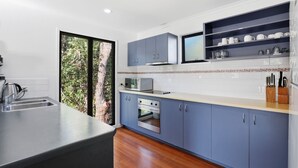 A modern kitchen with blue cabinets, a built-in oven, a microwave, and a sink. - Straddie Beach House 2 | Bush & Beach Retreat (Point Lookout)