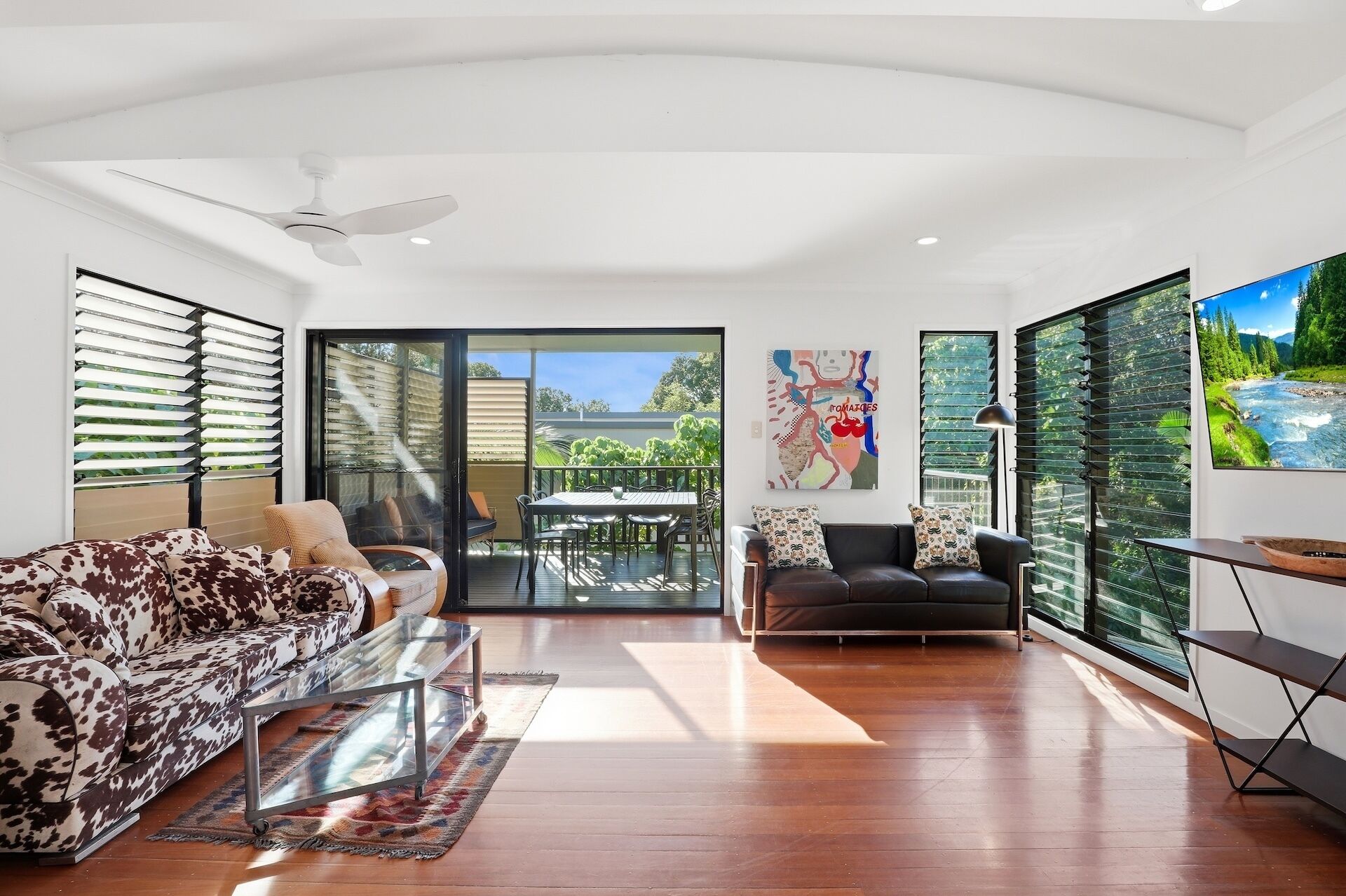 A spacious living room with a sofa, a black leather couch, a glass coffee table, and a dining area with a table and chairs.