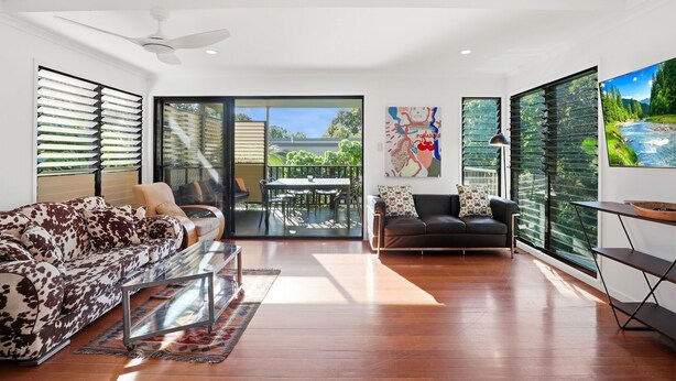 A spacious living room with a sofa, a black leather couch, a glass coffee table, and a dining area with a table and chairs. - Straddie Beach House 2 | Bush & Beach Retreat (Point Lookout)