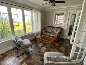 Una habitación con sofá, sillón, mesa de centro y ventanas amplias con cortinas.