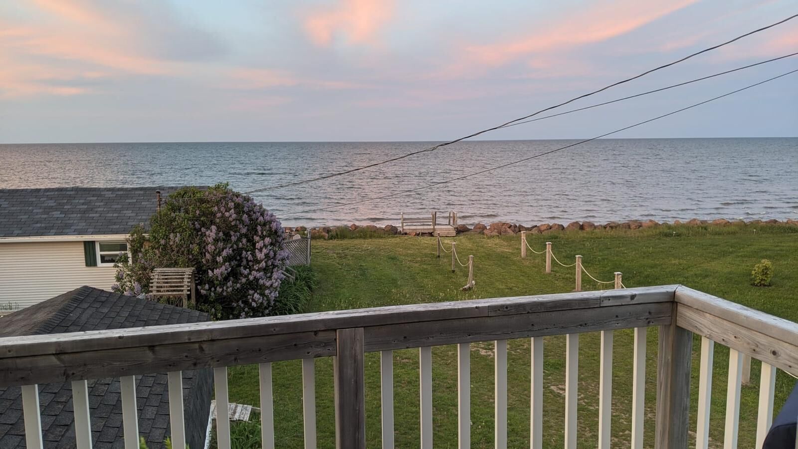 A wooden deck with a view of the sea and a grassy area with a fence.