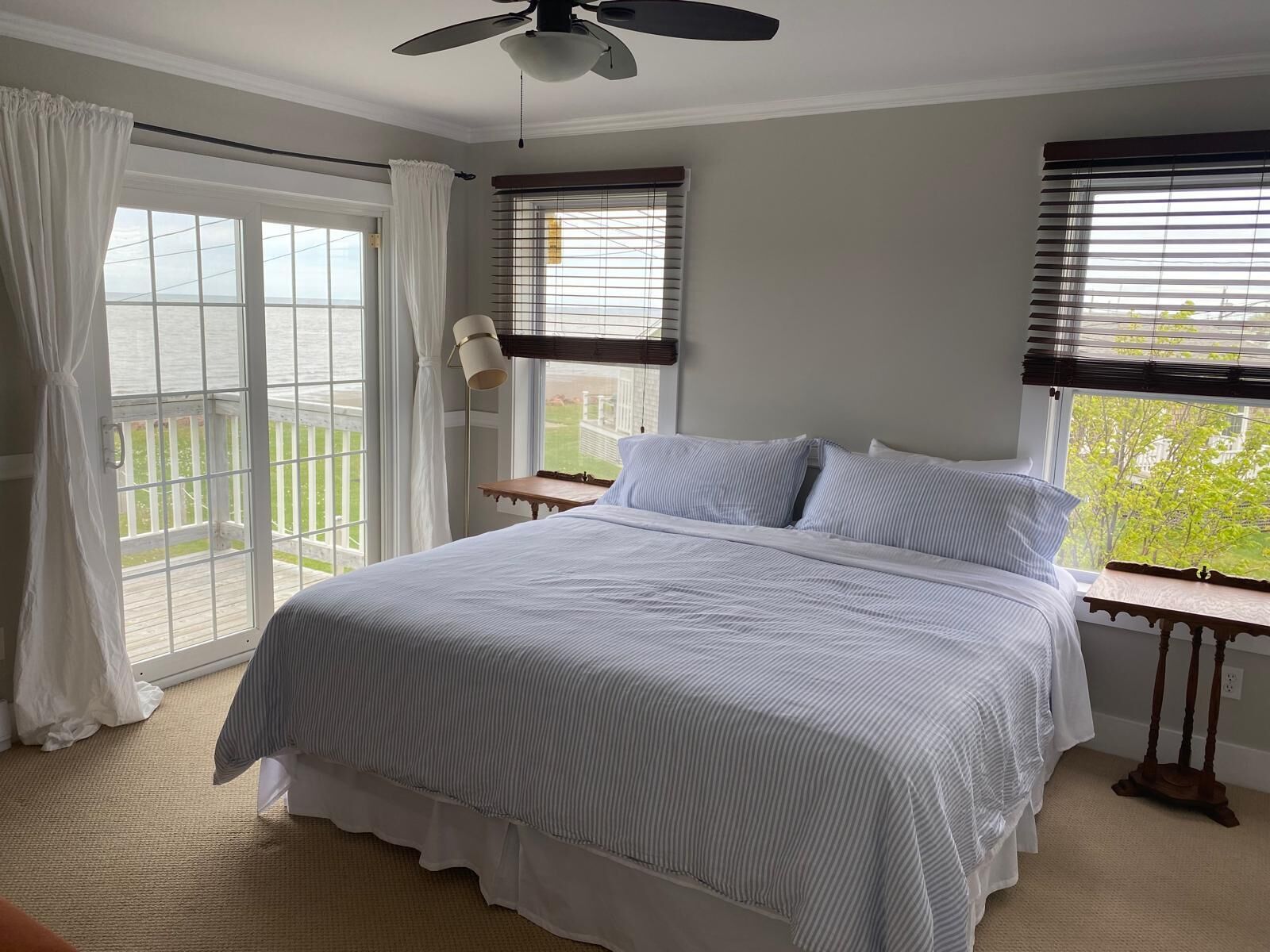 A bedroom with a bed, a ceiling fan, a window with blinds, and a view of the outdoors.