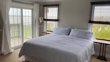 A bedroom with a bed, a ceiling fan, a window with blinds, and a view of the outdoors.