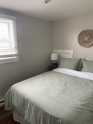 Un dormitorio con cama, lámpara de noche, un adorno en la pared y ventana con persianas.