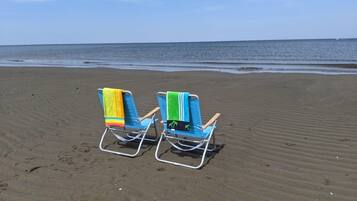Two beach chairs with towels on a sandy beach.