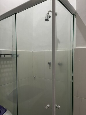 A glass-enclosed shower with a handheld showerhead, a glass door, and a tiled wall. - Studio vista mar pertinho da praia (Rio de Janeiro)