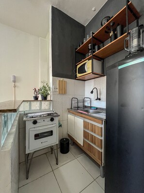A compact kitchen with a stove, microwave, sink, and wooden cabinets. - Studio vista mar pertinho da praia (Rio de Janeiro)