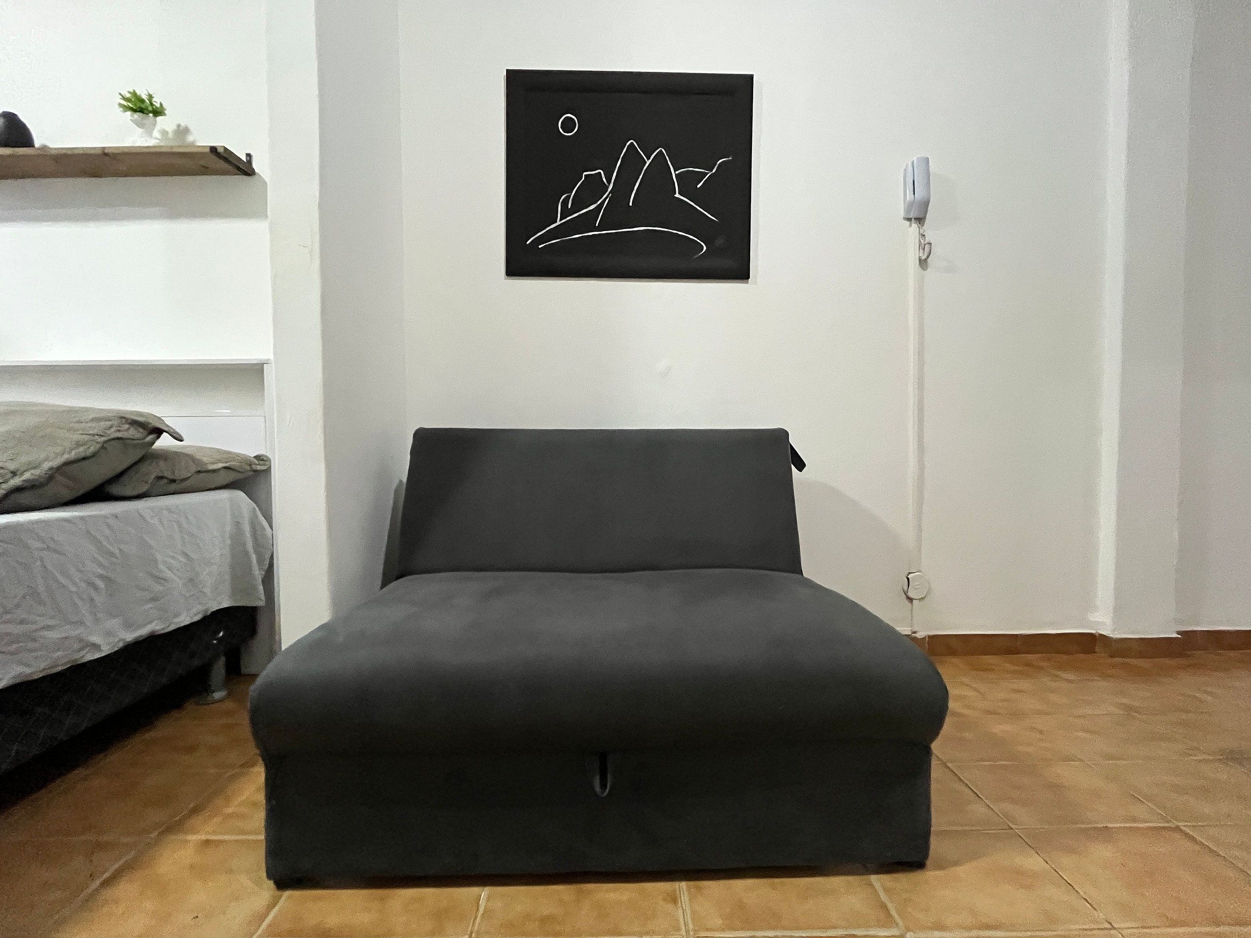 A room with a bed, a sofa, a wall-mounted picture, and a wall socket.