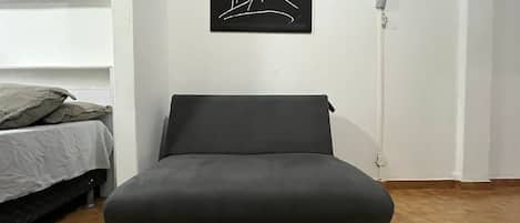 A room with a bed, a sofa, a wall-mounted picture, and a wall socket.