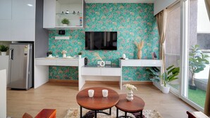 A modern kitchen with a teal floral wallpaper, a flat-screen TV, a refrigerator, and a dining area with two chairs and a small table.