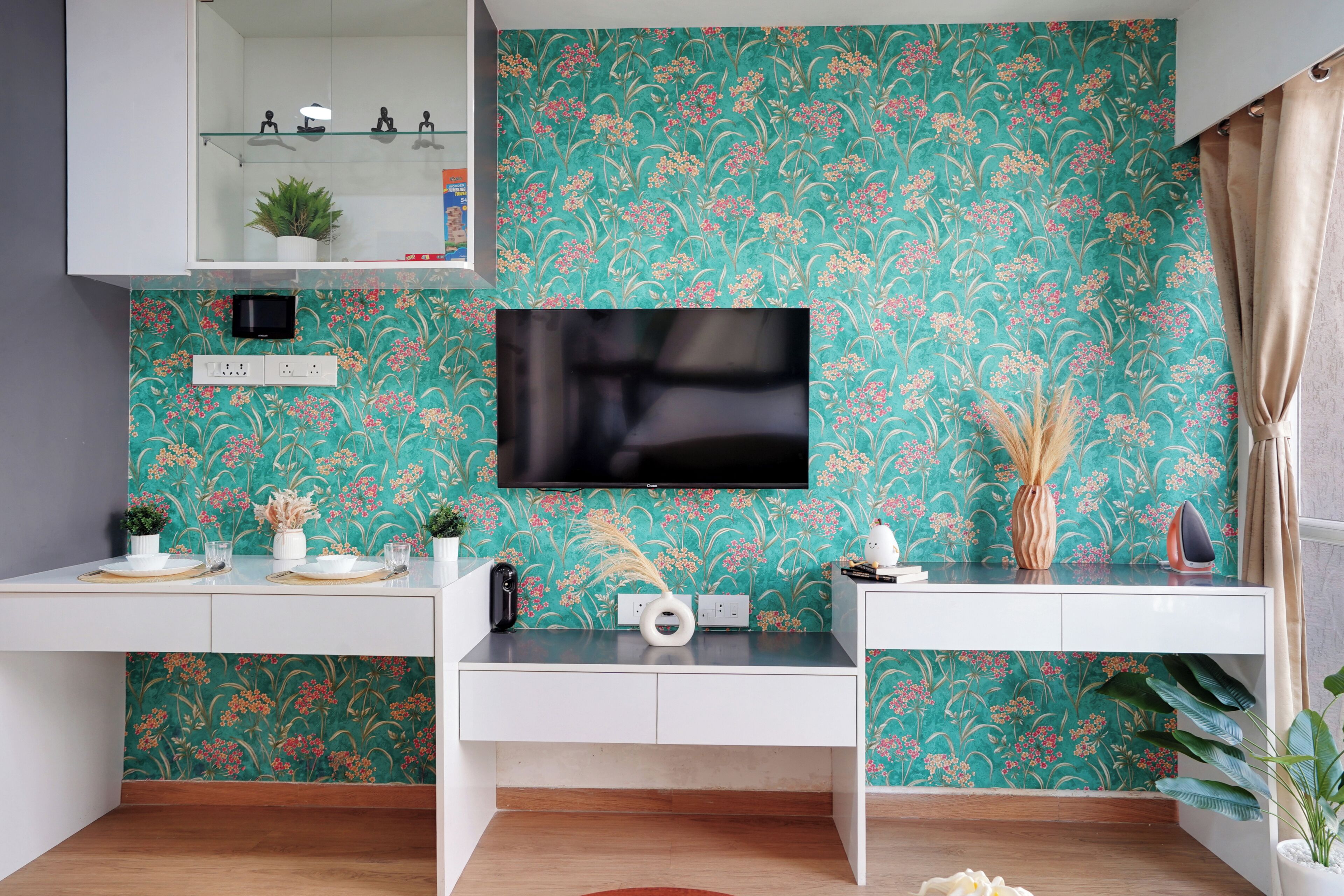 A modern kitchen with a teal floral wallpaper, a flat-screen TV, white cabinetry, and a built-in oven.