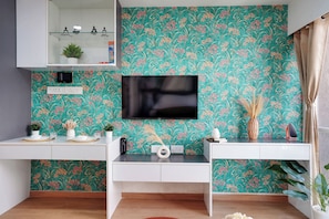 A modern kitchen with a teal floral wallpaper, a flat-screen TV, white cabinetry, and a built-in oven.