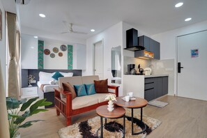 A modern living room with a sofa, coffee table, and a small kitchen area with a stove and cabinets.