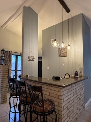 A kitchen with a central island, bar stools, hanging pendant lights, and a decorative sign. - 3-bedroom house in charming Houston with cool AC (Houston)