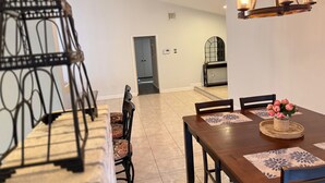 A dining area with a wooden table, chairs, and a chandelier. There is a door leading to another room.