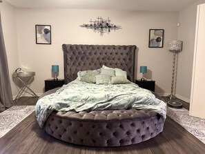 A round, tufted bed with a grey headboard in a bedroom with two bedside tables, a floor lamp, and artwork on the walls. - 3-bedroom house in charming Houston with cool AC (Houston)