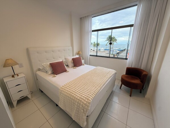 A bedroom with a bed, a nightstand, a chair, and a window with a view.