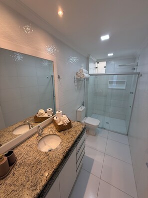 Un baño moderno con encimera de granito, dos lavamanos, cabina de ducha con mampara de vidrio y un inodoro.