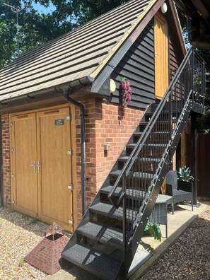 A building with a brick facade, a wooden door, a metal staircase, and a small outdoor seating area. - Treetop Private  studio (tiny house) (Farnborough)