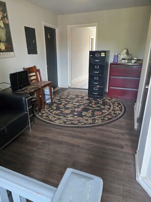 A room with a dark wood floor, a black leather sofa, a wooden chair, a desk with a computer, a red filing cabinet, and a floral rug. - Tranquil Studio apartment with AC in charming Camden near Philadelphia (Camden)
