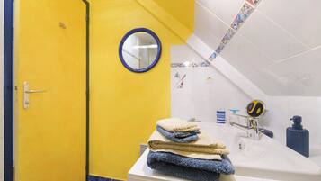 Une salle de bain avec une porte jaune, un lavabo blanc avec un robinet bleu, un miroir et une pile de serviettes.