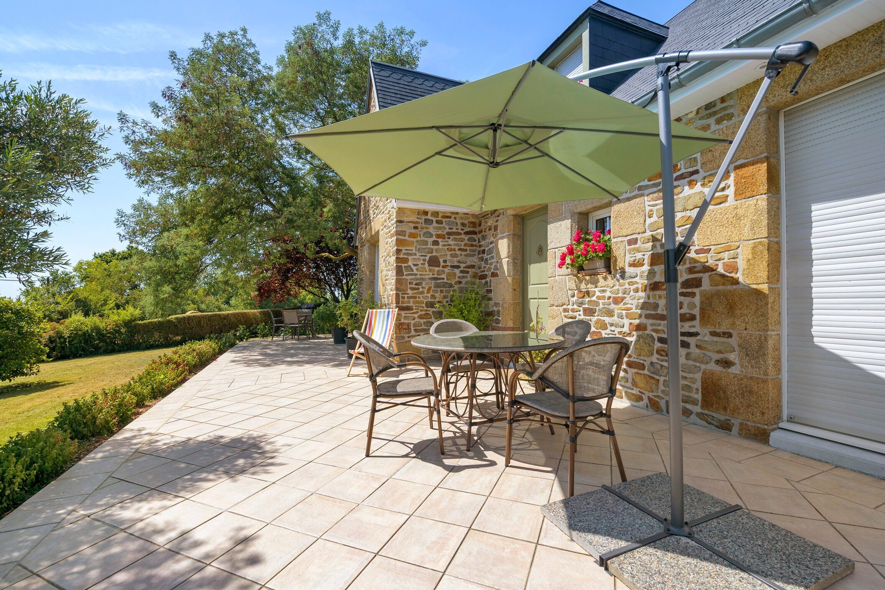 A patio with a table and chairs, a green umbrella, and stone walls.
