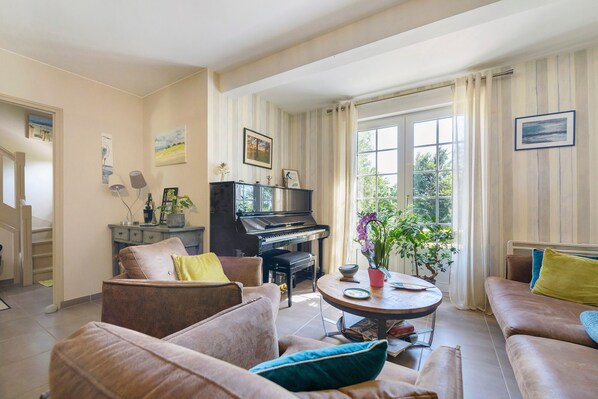 Un salon avec un piano, des canapés, une table basse et une fenêtre avec des rideaux.