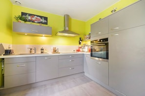 A modern kitchen with grey cabinets, a stainless steel oven, and a yellow accent wall.