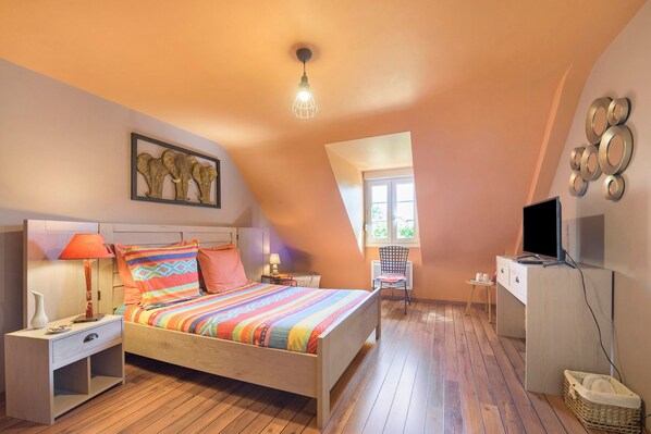 A bedroom with a bed, nightstand, lamp, artwork, and a television.