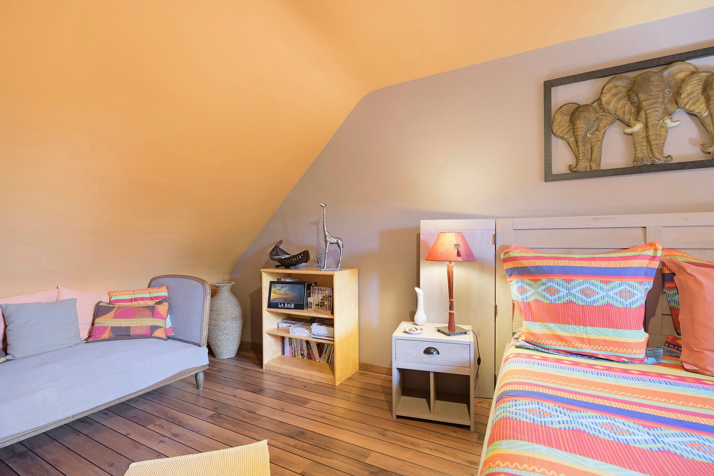 Une pièce confortable avec un canapé, un lit, une table de chevet, une lampe, une bibliothèque et un tableau encadré au mur.