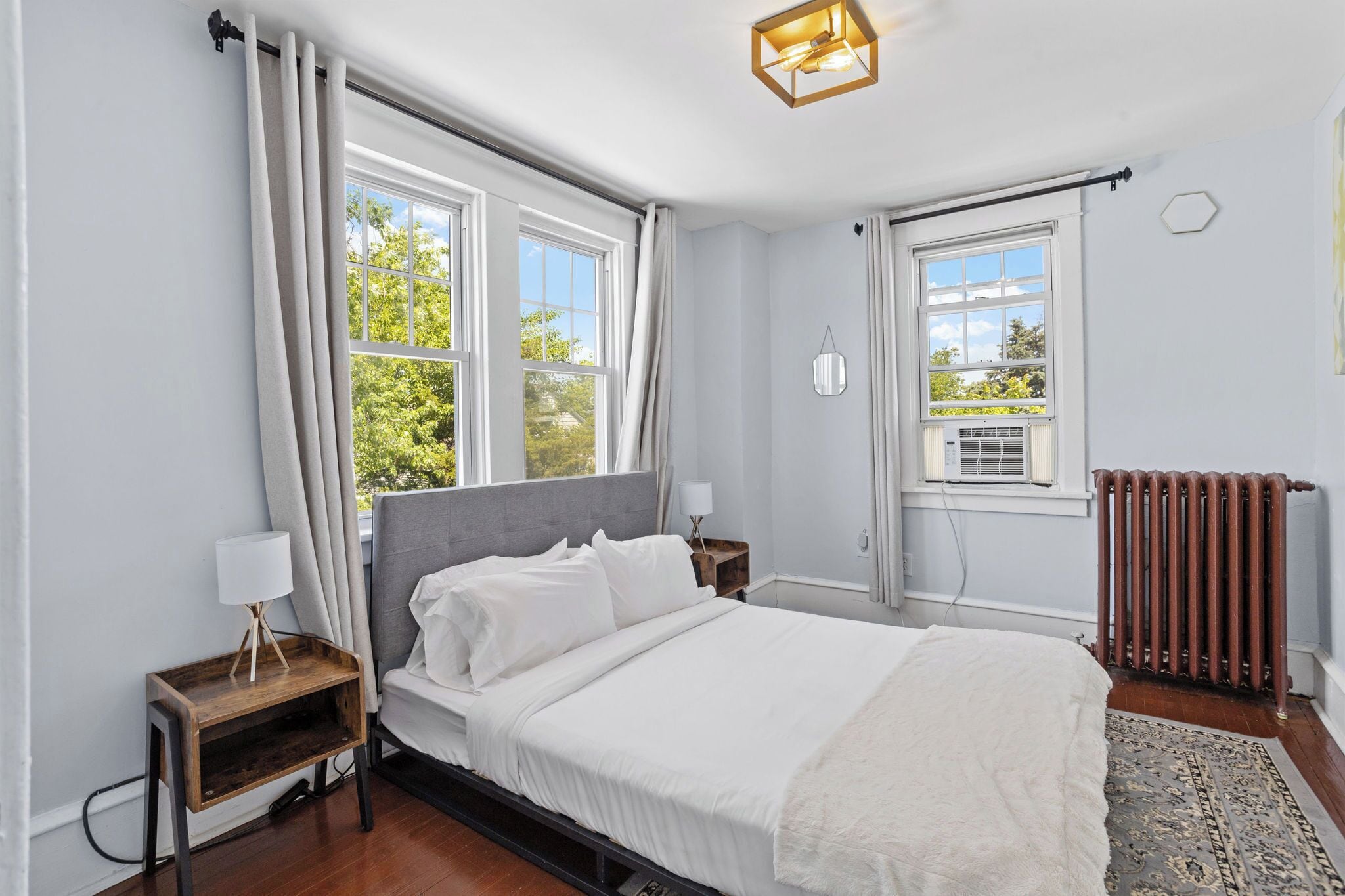 A bedroom with a bed, bedside tables, a radiator, and large windows.