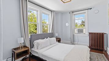A bedroom with a bed, bedside tables, a radiator, and large windows.