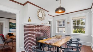 Uma sala de jantar com lareira de tijolos, mesa de madeira e cadeiras cinzentas.