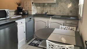 Een functionele keuken met een magnetron, broodrooster en vaatwasser, een eettafeltje met stoelen en een betegelde spatwand.