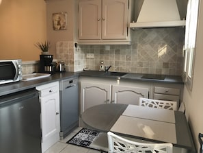 A compact kitchen with a microwave, toaster, and dishwasher, a small dining table with chairs, and a tiled backsplash. - Cottage "Little House in Coulon, Marais Poitevin" (Coulon)