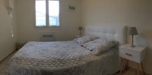 A bedroom with a bed, two bedside lamps, a window, and a radiator. - Cottage "Little House in Coulon, Marais Poitevin" (Coulon)