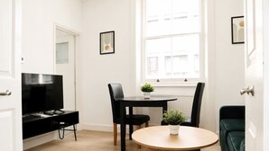 Ein modernes Wohnzimmer mit Fernseher, Esstisch, Stühlen, einer kleinen Pflanze und einem grünen Sofa.