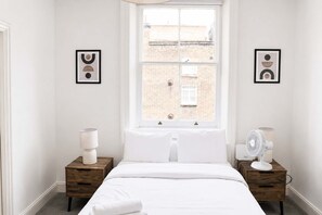 Ein Schlafzimmer mit großem Fenster, einem Bett, zwei Nachttischen mit Lampen und zwei gerahmten abstrakten Kunstwerken.