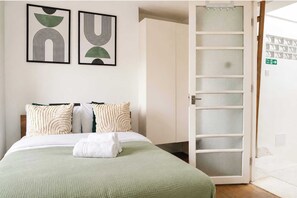 A hotel room with a bed, pillows, a green blanket, and two framed abstract artworks on the wall. - Elegant 1BR, Fitzrovia, Steps from West End (London)
