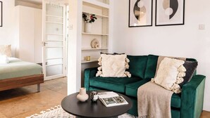 Habitació amb un llit, un sofà verd, una taula petita amb un vas i una revista, i un armari blanc amb prestatges.