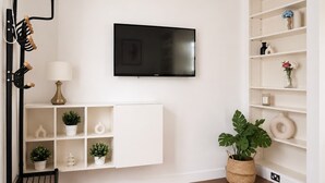 Un saló modern amb televisió de pantalla plana, mobles de prestatgeries blanques, una planta en test i una cadira negra.