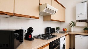 Een moderne keuken met een magnetron, koffiezetapparaat, gasfornuis, wasmachine en vaatwasser.